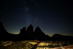 Die drei Zinnen in der Nacht. Unten sieht man das rote Licht der Stirnlampe eines Fotografen